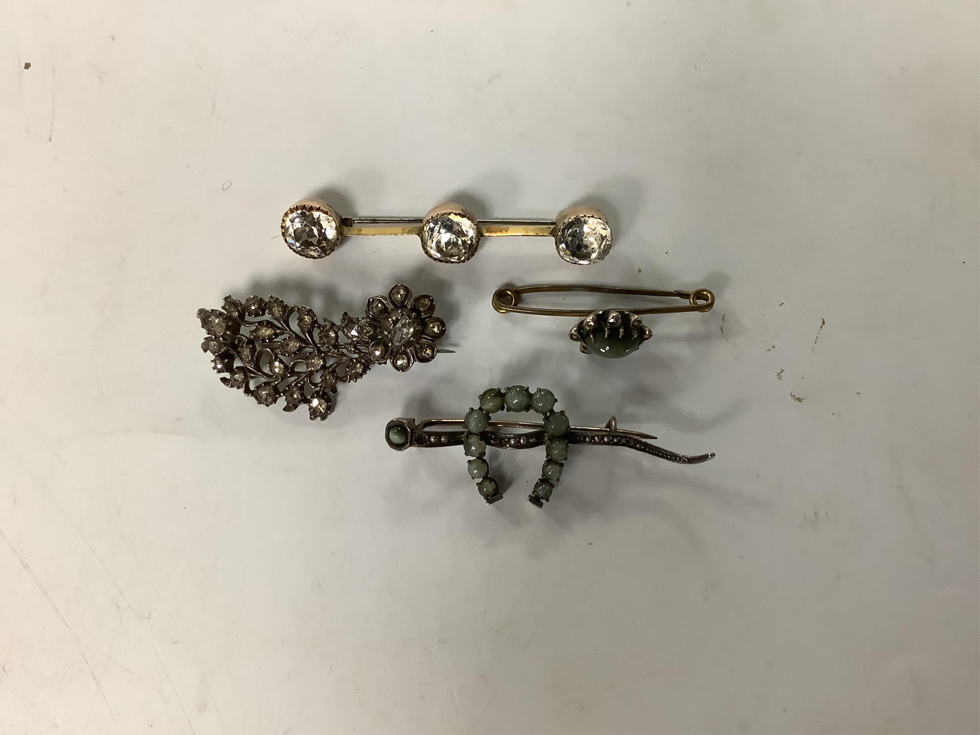 A white metal and rose-cut diamond cluster set floral brooch, 42mm, a cat's eye quartz and rose cut diamond set bar brooch, one other cat's eye quartz set horseshoe brooch and a three stone white paste set bar brooch.